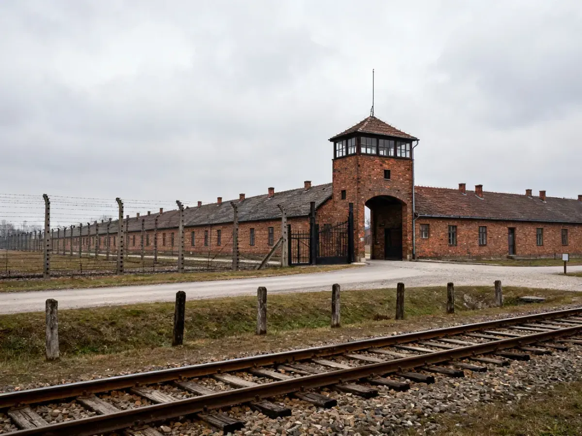 Droga i tory prowadzące do bramy Auschwitz-Birkenau, puste baraki i ogrodzenia tworzące poważną, refleksyjną atmosferę.