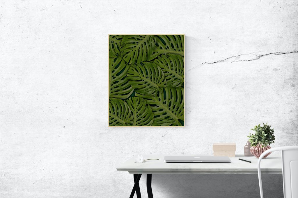 stylowe obrazy do salonu, pomieszczenie z biurkiem na którym leży macbook, a na ścianie wisi obraz z zielonymi liścmi wodnymi